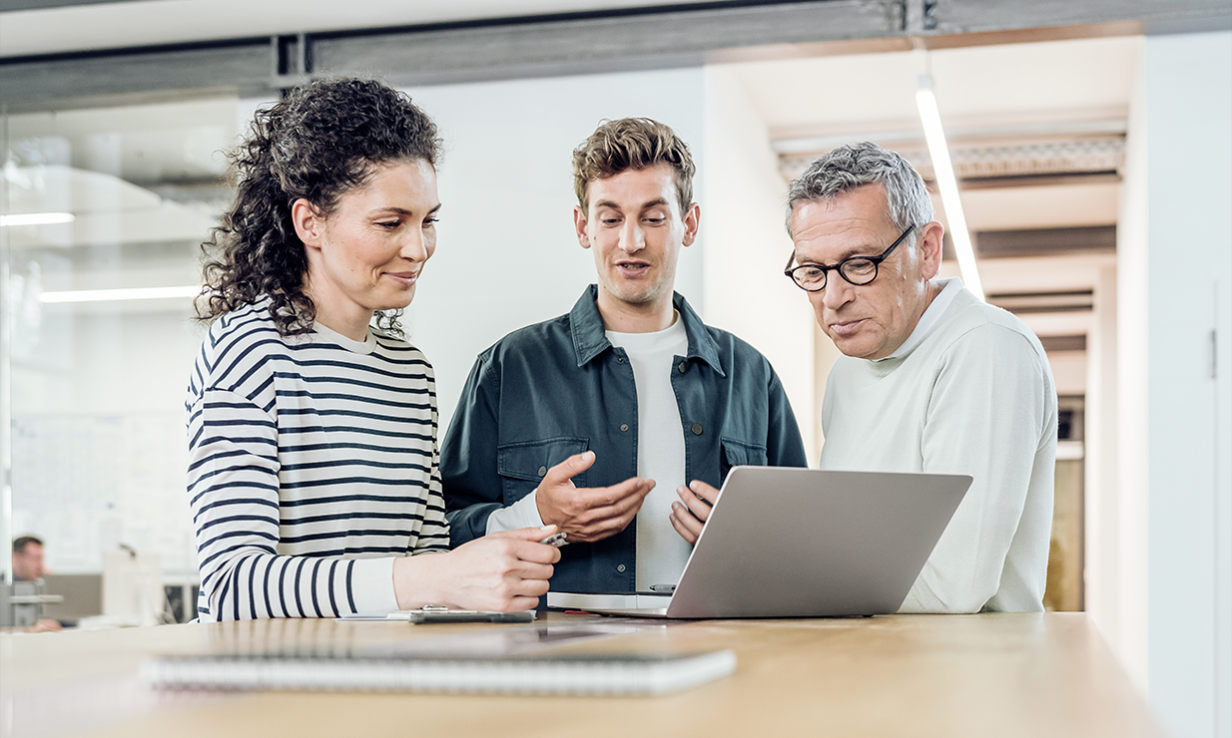 Eine Frau und zwei Männer schauen gemeinsam auf einen Laptop