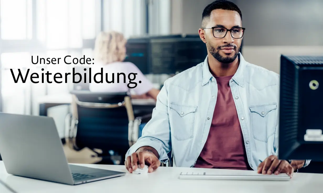 Ein junger Mann sitzt am Computer, neben ihm steht ein Laptop. Im Hintergrund sitzt eine Frau vor einem Bildschirm, auf dem Codes zu sehen sind.