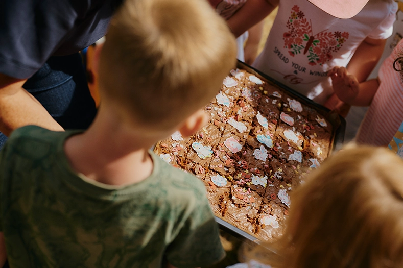 Mehrere Kinder stehen im Kreis um ein Blech mit einem Schokokuchen, der bunt mit Einhornfiguren dekoriert ist.