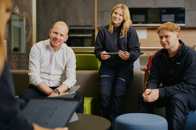 Björn Brendemühl sitzt mit zwei jungen Kollegen in einem Besprechungsraum. Alle lächeln freundlich in die Kamera.