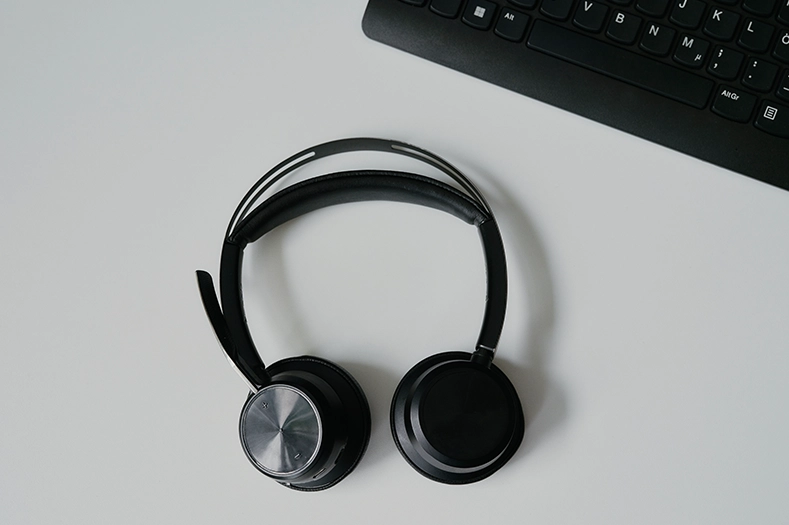 Auf einer weißen Oberfläche ist ein schwarzes Headset sowie Tasten einer Tastatur zu sehen. 