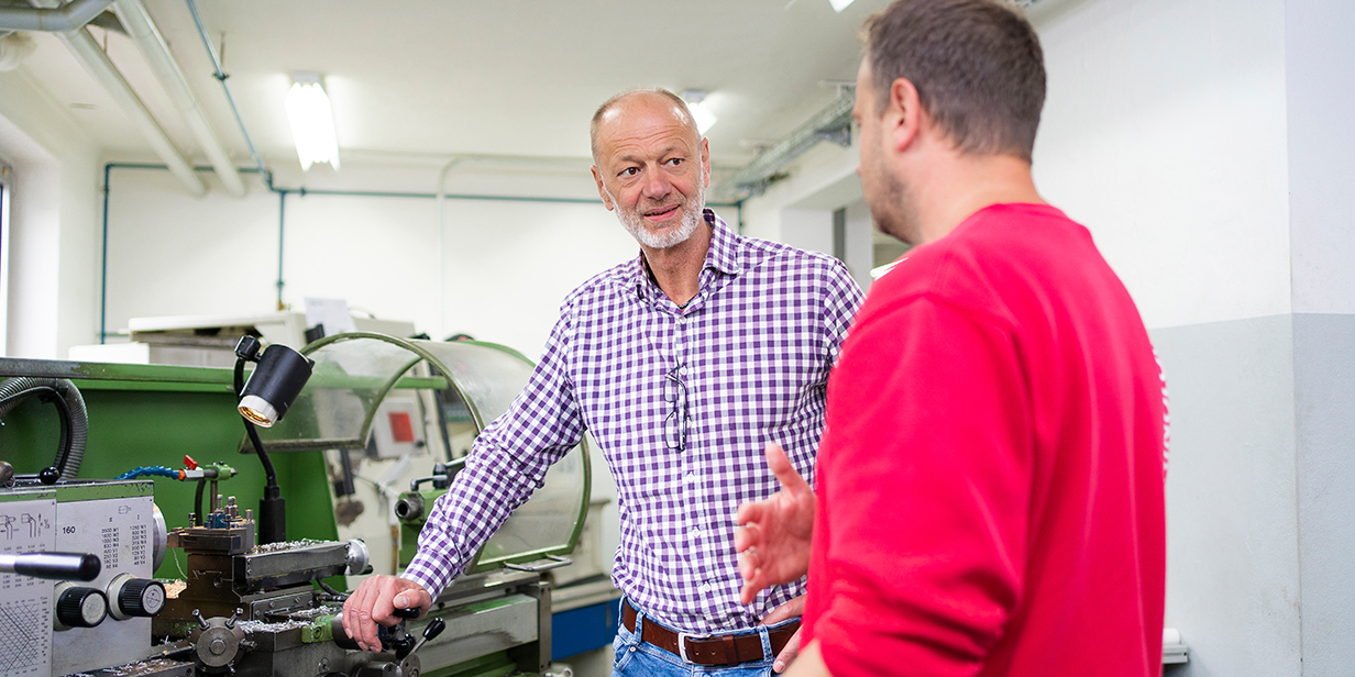 Ralf Greif, Personalleiter der Bauer Unternehmensgruppe GmbH aus Oberbayern, und ein Mitarbeiter unterhalten sich vor einer Maschine.
