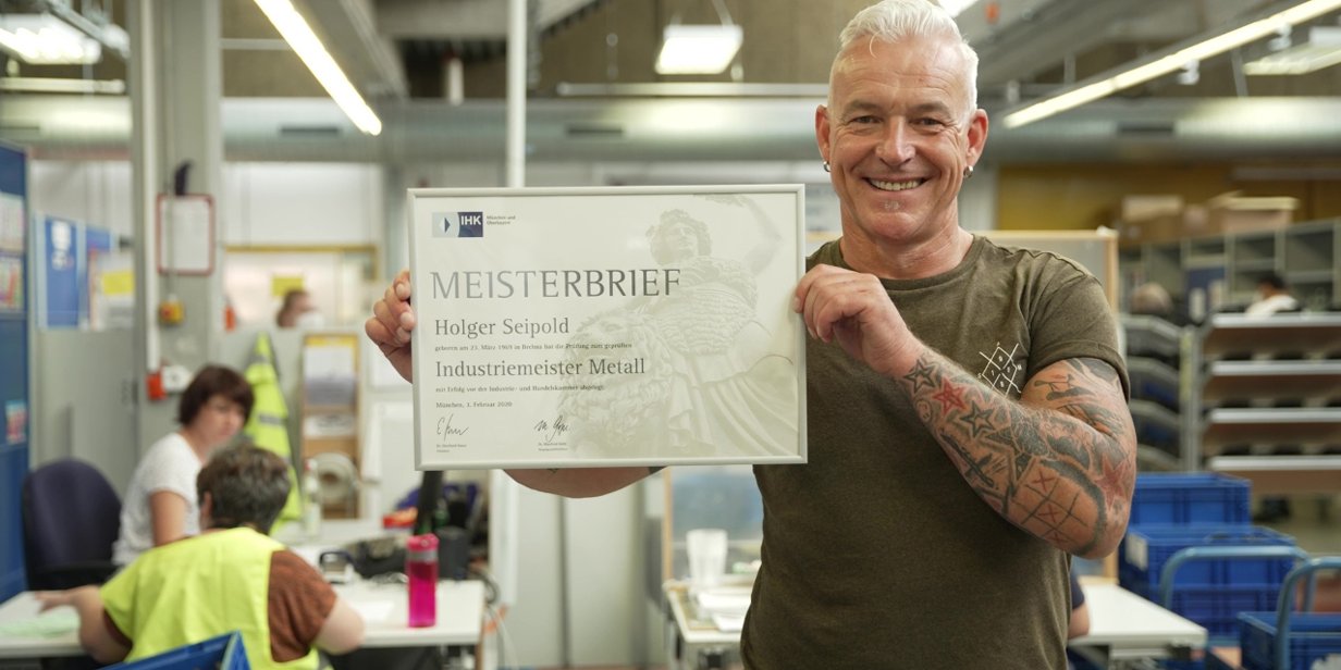 Holger Seipold hält lächelnd seinen Meisterbrief in die Kamera.