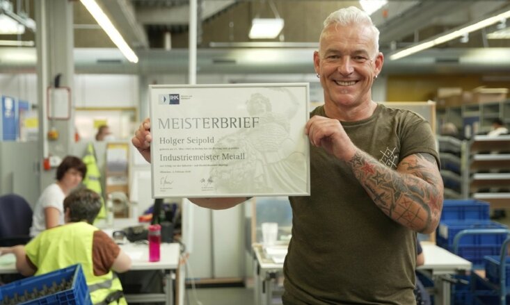 Holger Seipold hält seinen Meisterbrief in der Hand und lächelt. 