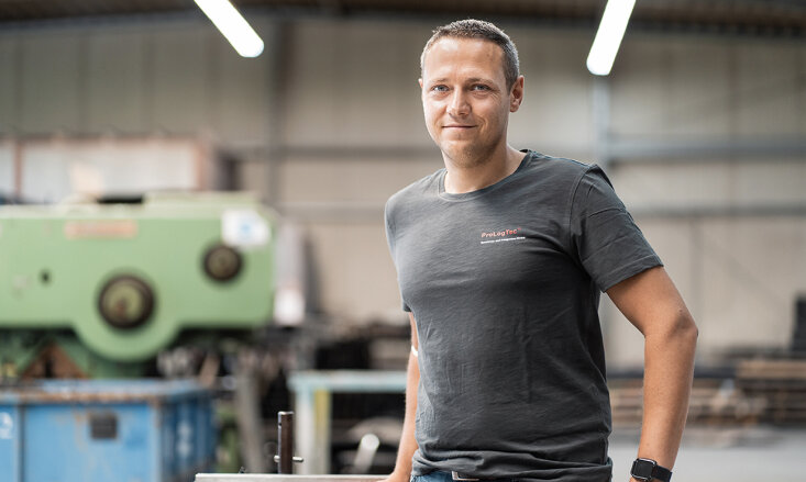 Christian Gundermann trägt ein Firmen-T-Shirt mit der Aufschrift Prologtec und steht in einem Maschinenraum.