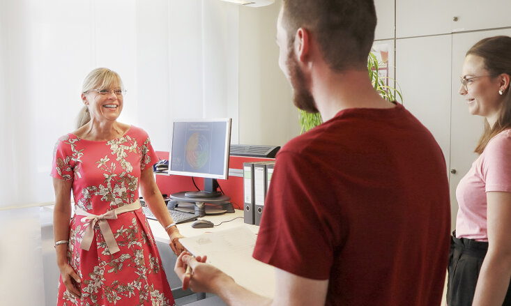 Drei lächelnde Personen stehen in einem Büro unter unterhalten sich.