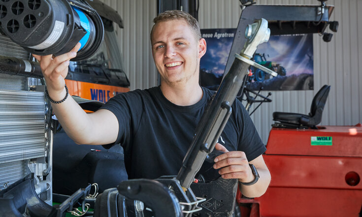 Tim Wolf steht an einer Maschine und lächelt.