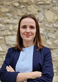 Olga Tissot, eine junge Frau steht mit verschränkten Armen und lächelt in die Kamera.